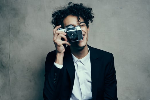 curly-haired man in a classic suit looks at the camera in his hand studio hobby photo