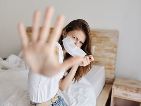 irritable woman covers herself with her hands from the camera and sits on the bed indoors photo