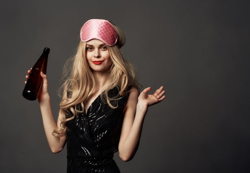 Drunk woman with a bottle in her hand black dress pink sleep mask photo