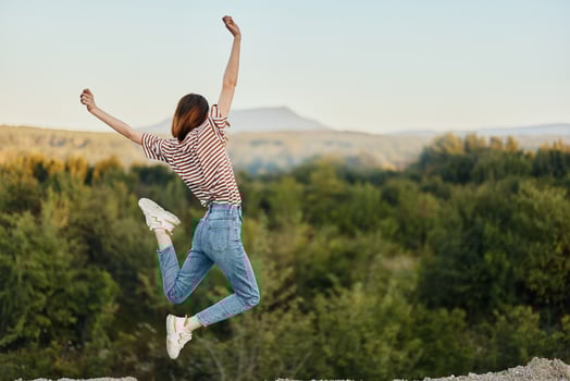 Happy woman jumping up from happiness in nature with her back to the camera with a beautiful mountain view photo