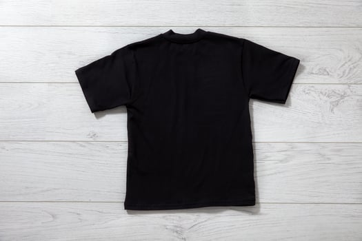 Back views on boys t-shirts on white wooden desk background. Mockup for design closeup photo