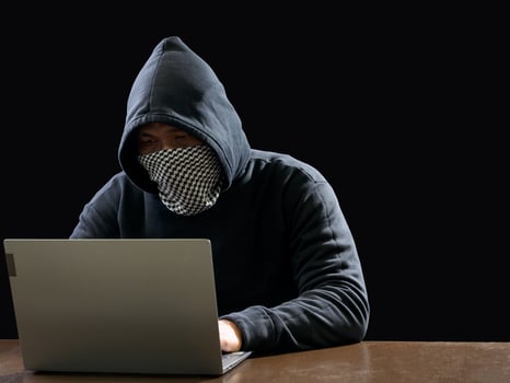 Hacker spy man one person in black hoodie sitting on a table looking computer laptop used login password attack security to circulate data digital in internet network system, night dark background. photo