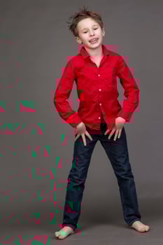 Handsome boy in a red shirt and jeans on a gray background. A child in the modeling business is posing. photo