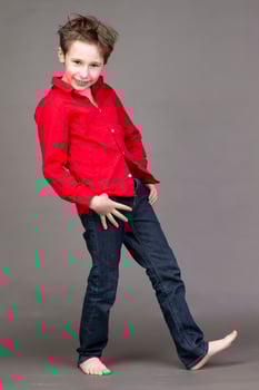 Handsome boy in a red shirt and jeans on a gray background. A child in the modeling business is posing. photo