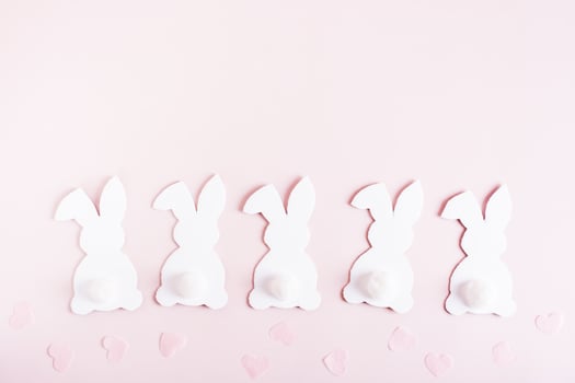 Happy easter white cardboard bunnies in a row and hearts on pink background top view photo