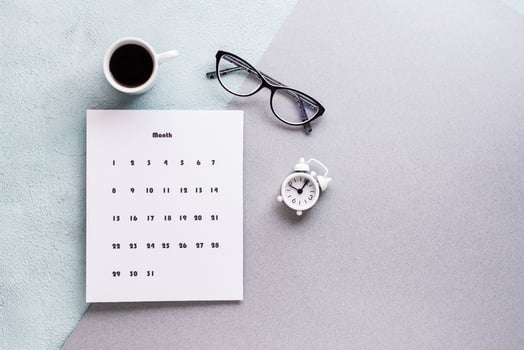 Blank sheet of monthly calendar, coffee cup, alarm clock and glasses on textured background. Time planning and organization photo