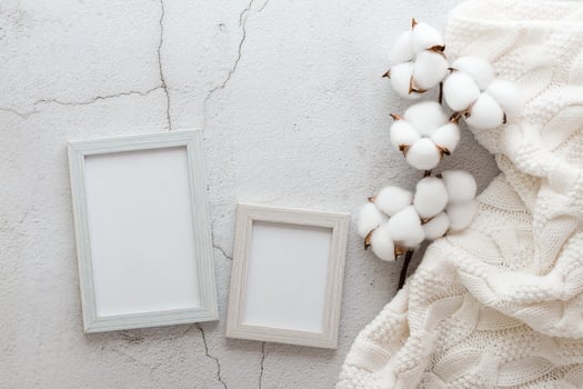 Eco friendly homemade template knitted sweater, cotton branch and two empty photo frames on a gray background. Pastel shades