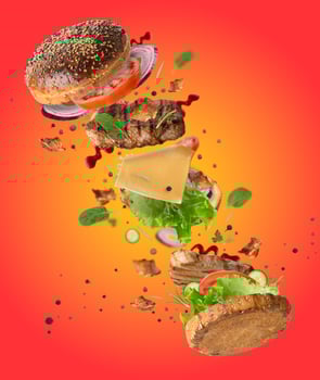 Delicious burger with flying ingredients, pieces of vegetables, spices and meat fried steak on orange background photo