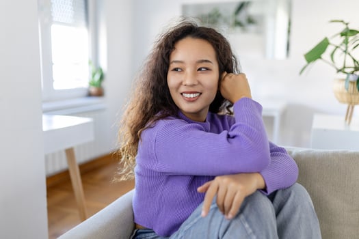 Happy Asian woman sitting on sofa at home and looking at camera. Portrait of comfortable woman in winter clothes relaxing on sofa . Portrait of beautiful woman smiling and relaxing during autumn. photo