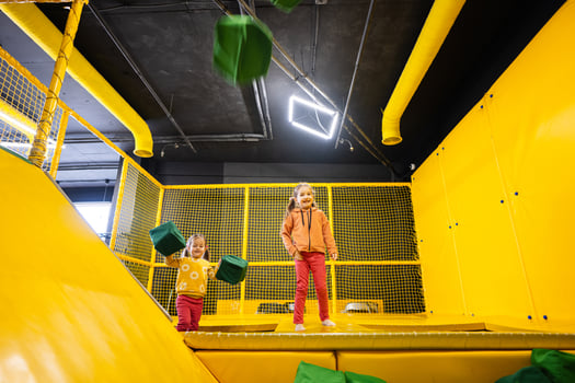 Siblings throwing soft cubes at yellow playground park. Sisters in active entertaiments. photo