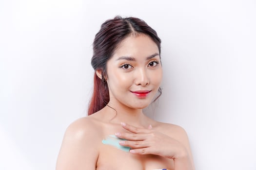 Skin Care Products Concept. Asian woman applying moisturizing lotion on body after shower, standing wrapped in towel, cropped image photo