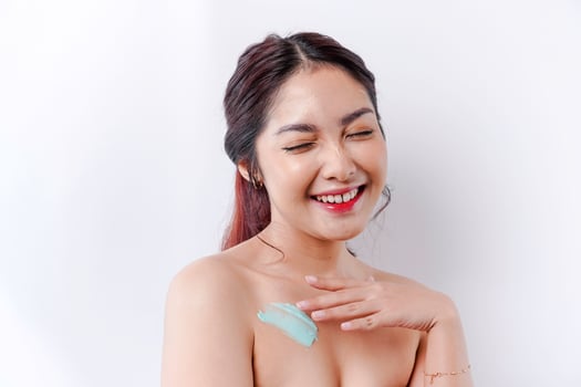Skin Care Products Concept. Asian woman applying moisturizing lotion on body after shower, standing wrapped in towel, cropped image photo