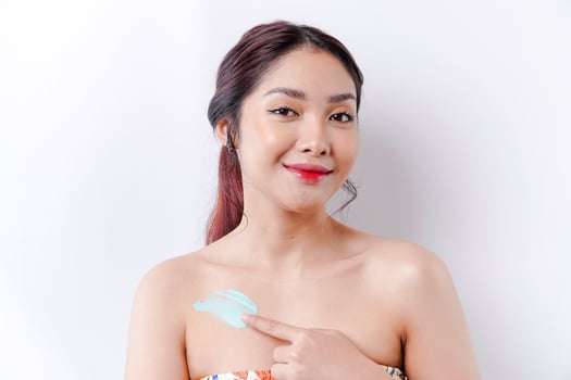 Skin Care Products Concept. Asian woman applying moisturizing lotion on body after shower, standing wrapped in towel, cropped image photo