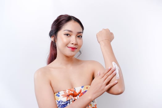 Skin Care Products Concept. Asian woman applying moisturizing lotion on body after shower, standing wrapped in towel, cropped image photo