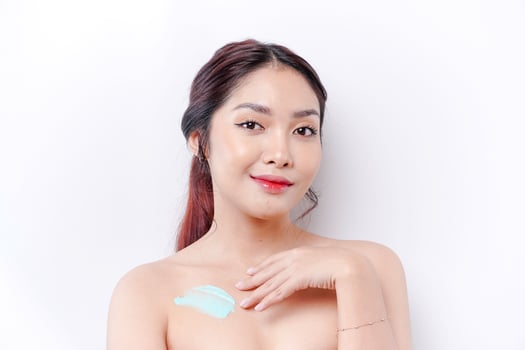 Skin Care Products Concept. Asian woman applying moisturizing lotion on body after shower, standing wrapped in towel, cropped image photo