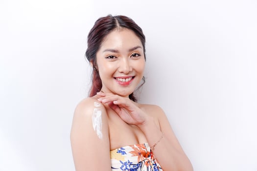 Skin Care Products Concept. Asian woman applying moisturizing lotion on body after shower, standing wrapped in towel, cropped image photo