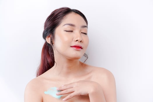 Skin Care Products Concept. Asian woman applying moisturizing lotion on body after shower, standing wrapped in towel, cropped image photo