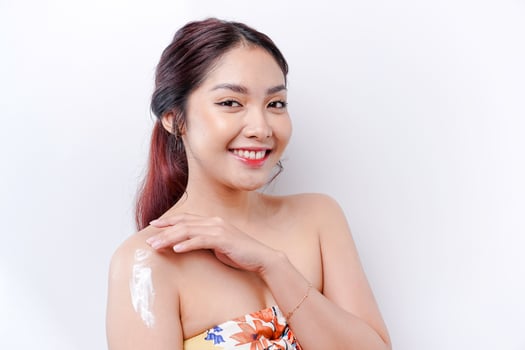 Skin Care Products Concept. Asian woman applying moisturizing lotion on body after shower, standing wrapped in towel, cropped image photo