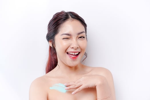 Skin Care Products Concept. Asian woman applying moisturizing lotion on body after shower, standing wrapped in towel, cropped image photo