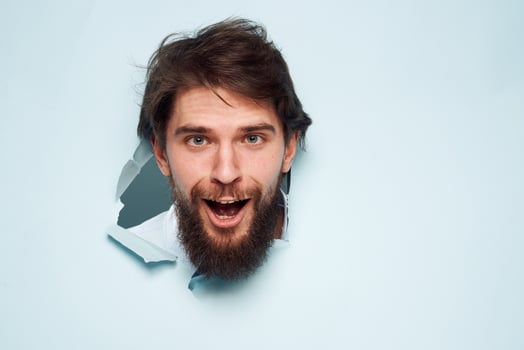 Cheerful bearded office work man peeps out from behind the wall photo