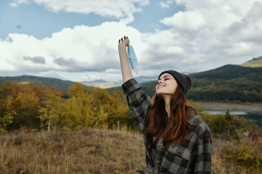 Happy woman in the mountains raised her hand up and a medical mask photo