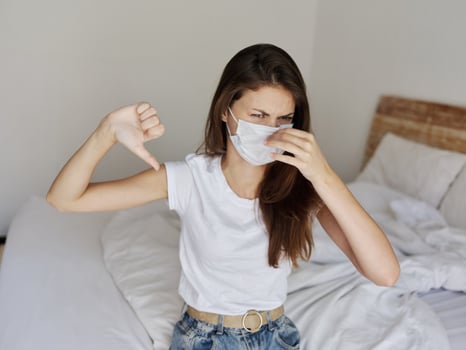 upset woman showing thumb down medical mask in bedroom photo