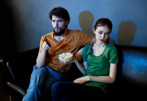 A woman and a man with popcorn on a leather sofa indoors watching TV in the evening photo