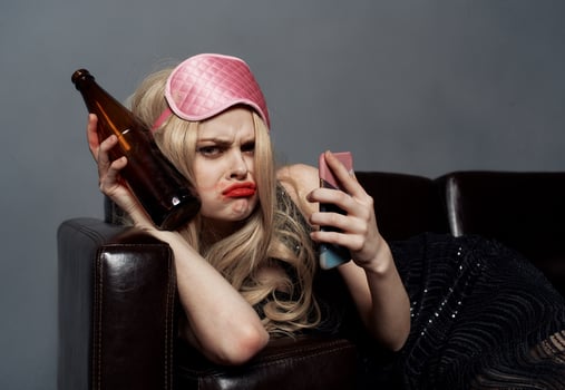 A woman in a pink mask lies on the couch with a bottle of beer and a phone in her hand photo