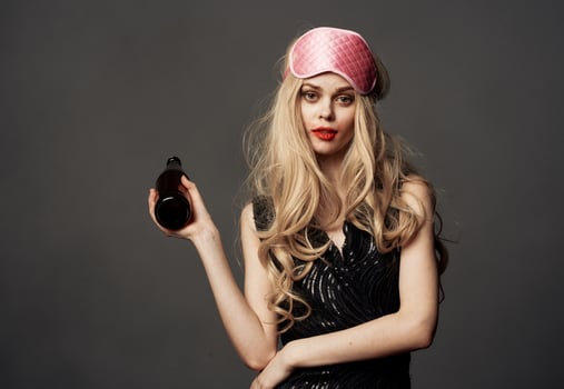 Women with a pink sleep mask holds a bottle of beer in her hand photo
