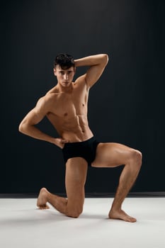 a sporty man with a naked body in black panties on a dark background is on his knee photo