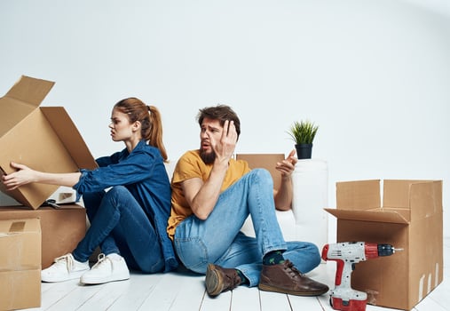 man and woman sitting on the floor with their backs to each other renovation work moving a flower in a pot photo