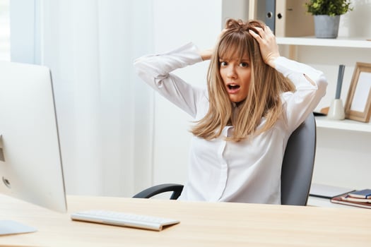 Shocked adorable blonde businesswoman typing answer for client look at camera touch head sitting at workplace in modern office. Unhappy employee work on computer online in support service. Copy space photo