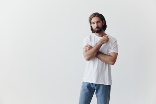 Portrait of a man with a black thick beard and long hair in a white T-shirt on a white isolated background emotion of sadness and longing photo