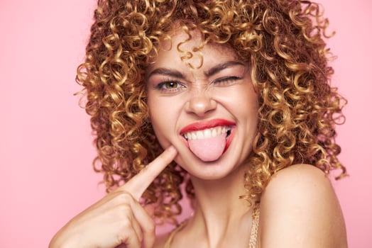 Charming model touches his face with his finger and shows his tongue sequin shirt pink background photo
