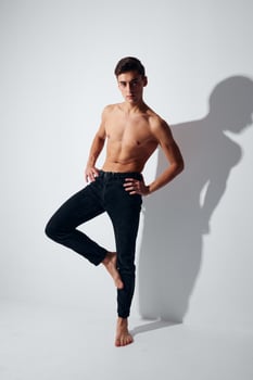 A man in trousers and a naked torso stands on one leg against a light background photo