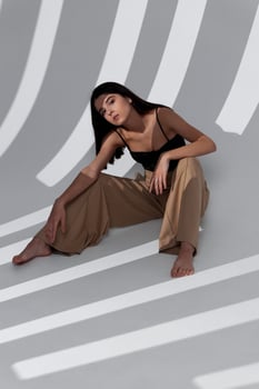 fashionable brunette in beige trousers sitting on the floor indoors and falling shadow on the wall photo