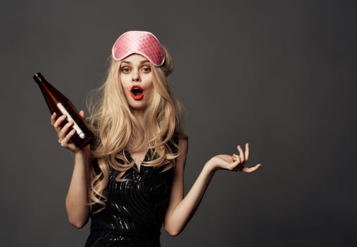 Woman with a bottle of beer on a gray background holidays sleep mask on her head photo
