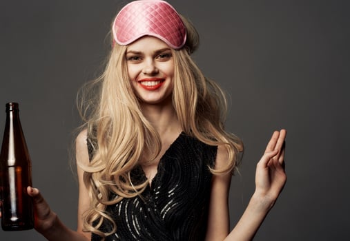 Women with a pink sleep mask holds a bottle of beer in her hand photo