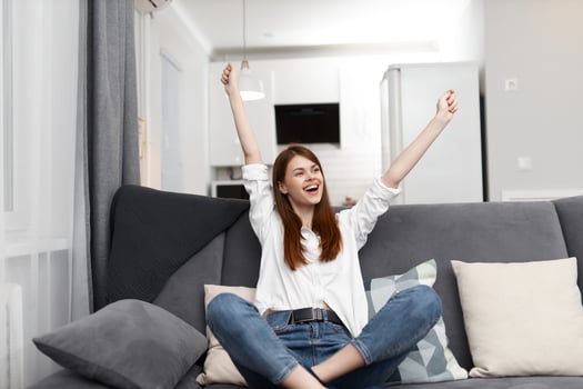 joyful woman with raised up arms sitting on sofa having fun and relaxing at home photo