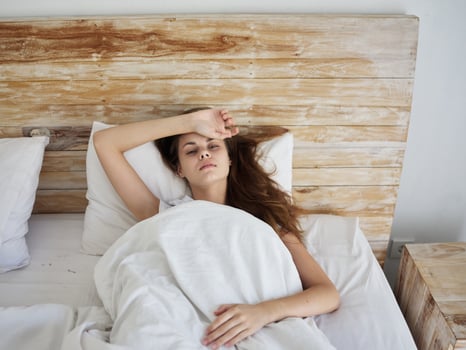 woman holding her hand on her forehead lying in bed feeling unwell photo