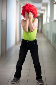 The child in a bright wig closed his eyes with his hands. photo