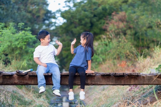 Cheerful children sitting on wooden bridge, Asian kids playing in garden, boy and girl reading books photo