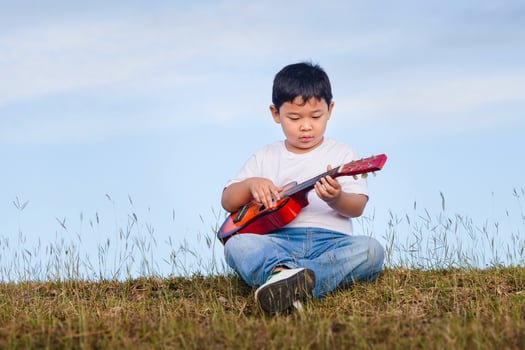 Portrait of Asian child boy playing outdoors. Happy boy with guitar having fun outdoor photo