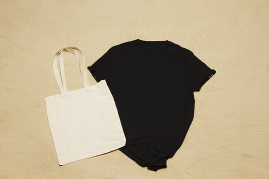 Mockup black summer t-shirt white shopper copy space. Sand beach texture background. Blank template shirt Top view. Summertime clothing. Flat-lay closeup tshirt on seashore. Beachtime holidays photo