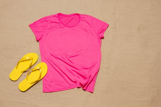 Sand beach texture background. Mockup pink summer t-shirt copy space. Blank template woman shirt Top view. Summertime accessories flip-flops. Flat-lay closeup tshirt on seashore. Beachtime photo