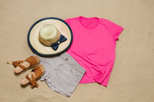 Sand beach texture background. Mockup pink summer t-shirt outfit copy space. Blank template woman shirt Top view. Summertime accessories hat, jeans. Flat-lay closeup tshirt on seashore. Beachtime photo