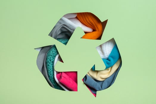 Second hand, circular fashion and recycling concept. Colorful clothes under paper cut recycling symbol photo