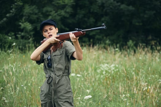 Woman on nature hunting with a gun in green overalls green leaves photo