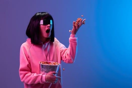 Excited awesome brunet woman in pink hoodie trendy specular sunglasses throws up popcorn look aside posing isolated in blue violet color light background. Neon party Cinema concept. Copy space photo