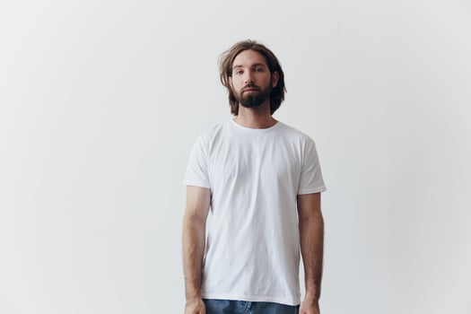 Portrait of a man with a black thick beard and long hair in a white T-shirt on a white isolated background emotion of sadness and longing photo